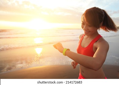 Health Sport Young Woman Run And Look Wear Smart Watch Device With Touchscreen On The Beach At Sunrise, Asian