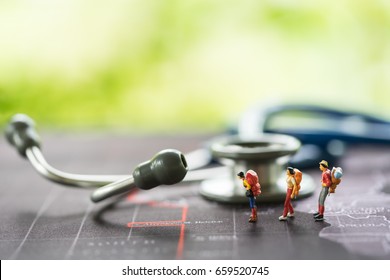 Health And Travel Insurance, Miniature People, Traveler With Backpack Walking In Front Of Stethoscope On World Map. Business, Health Care, And Traveling Concept.