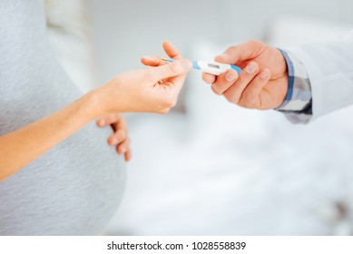 Health is of utmost importance. Scaled up look on a male pediatrician and an expectant woman standing next to each other and holding a thermometer.