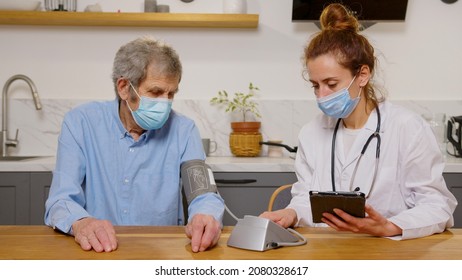 Health Visitor And A Senior Man During Home Visit. A Female Nurse Or A Doctor Examining A Man.