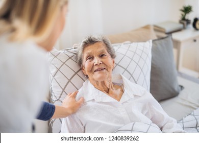 A Health Visitor Talking To A Sick Senior Woman Lying In Bed At Home.