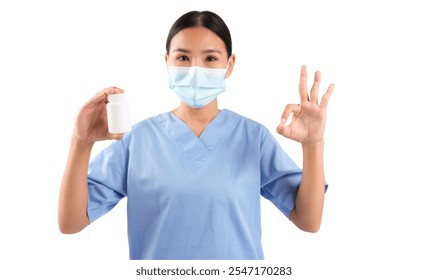 Health worker in blue scrubs holds a medicine bottle and shows an okay gesture, isolated on white background.