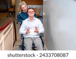 Health worker pushing a happy man with down syndrome using wheelchair while he gesturing success with fingers