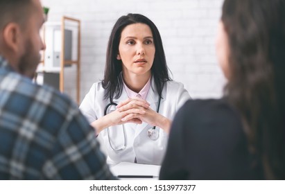 Healthcare And Assistance Concept. Doctor Listening To Patients, Explaining Symptoms To Young Family