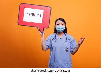 Healthcare Clinic Nurse Holding Cardboard Speech Bubble Sign While Wearing Protective Mask And Medical Uniform. Scared Nurse Wearing Stethoscope And Medical Clothing Asking For Help.