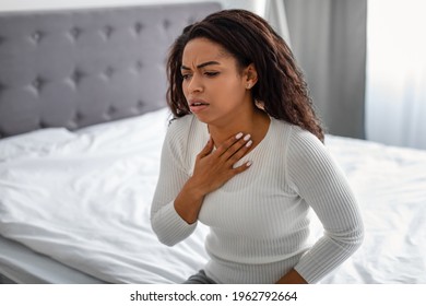 Healthcare, Cold And People Concept. Portrait Of Sad Sick Young Black Woman Coughing, Suffering From Sore Throat, Sitting In Bed At Home. Ill Lady Touching Neck With Hand, Free Copy Space