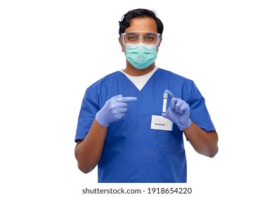 Healthcare, Coronavirus And Medicine Concept - Indian Doctor Or Male Nurse In Blue Uniform, Face Mask For Protection From Virus, Goggles And Gloves With Blood In Test Tube Over White Background