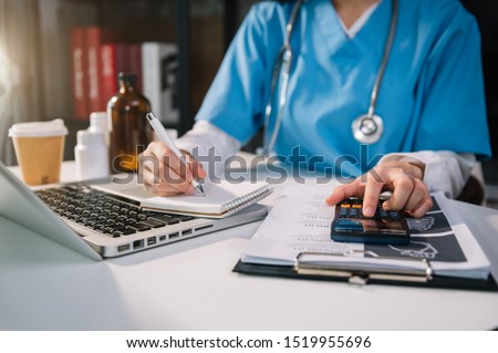 Healthcare costs and fees concept.Hand of smart doctor used a calculator and smartphone, tablet for medical costs at hospital in morning light
