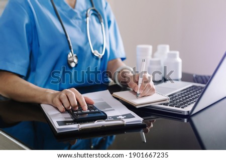 Healthcare costs and fees concept.Hand of smart doctor used a calculator and smartphone, tablet for medical costs at hospital 

