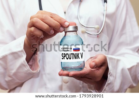 Healthcare cure concept with a hand in blue medical gloves holding Coronavirus, Covid 19 virus, Spoutnik V new russia vaccine vial