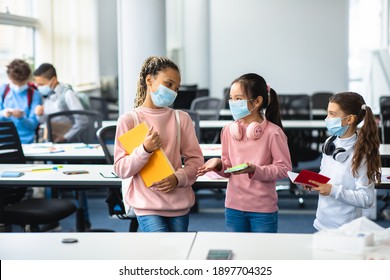 Healthcare, Education, Lifestyle And People Concept. Group of smiling diverse international pupils wearing medical face masks and headphones talking, standing with notebooks in classroom at school - Powered by Shutterstock