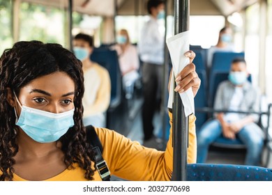 Healthcare And Epidemic Concept. African American Lady In Protective Face Mask Holding On Handle Using Tissue In Urban Bus, Avoid Touch Dirty Handrails. City Trip In Context Of Covid Pandemic