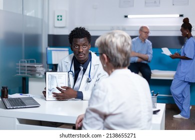 Healthcare Facility General Practitioner Presenting Medical Diagram To Senior Patient. Clinic Specialist Talking With Retired Woman About Health Risks And Clinical Problems While Showing Expertise