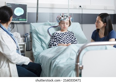 Healthcare hospital pediatric medic analyzing EEG scan of unwell little girl while in pediatric ward recovery room. Child patient wearing electroencephalography helmet while in pediatric clinic.