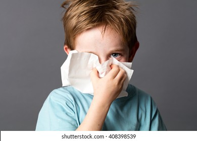 Healthcare Learning - Cute Little Child With Red Hair And Blue Eyes Hiding With A Tissue To Clean His Nose From A Cold Or Having Hay Fever, Grey Background Studio