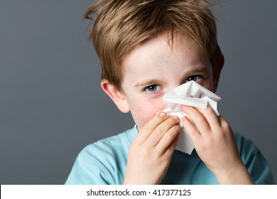 Healthcare Learning - Playful Little Child With Red Hair And Blue Eyes Using A Tissue To Clean His Nose From A Cold Or Having Pollen Allergies, Grey Background Studio