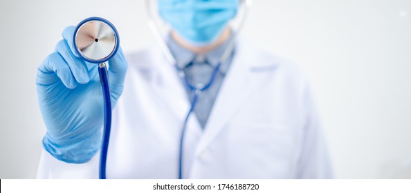 Healthcare and medical check up concept. Male Asian doctor holding stethoscope in hand. Physician man wearing surgical mask and gloves working in hospital clinic during Coronavirus (COVID-19) pandemic - Shutterstock ID 1746188720