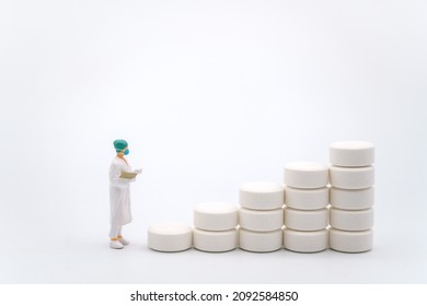 Healthcare And Medical Concept. Closeup Of Woman Doctor Miniature Figure With Patient File Looking To Stack Of White Pills On White Background.