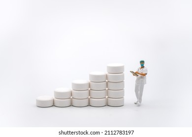 Healthcare And Medical Concept. Closeup Of Woman Doctor Miniature Figure With Patient File Looking To Stack Of White Pills On White Background.