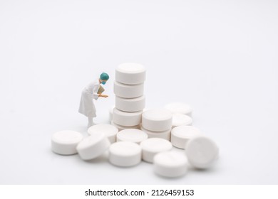 Healthcare And Medical Concept. Closeup Of Woman Doctor Miniature Figure With Patient File Looking To Stack Of White Pills On White Background.