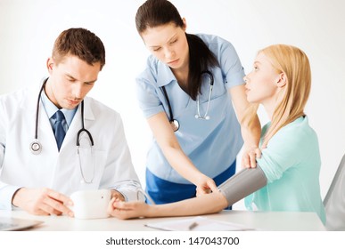 Healthcare And Medical Concept - Doctor And Nurse With Patient Measuring Blood Pressure In Hospital