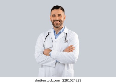 Healthcare, medical staff concept. Portrait of smiling male doctor posing with folded arms on grey studio background, free space. Professional general practitioner.