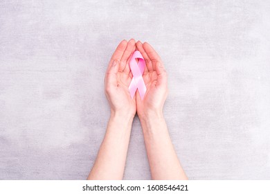 healthcare and medicine concept - female hands hold pink breast cancer awareness ribbon on gray background - Shutterstock ID 1608546421