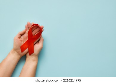 Healthcare and medicine concept - female hands holding red AIDS awareness ribbon on blue background. The symbol of The World AIDS Day or cancer or HIV Awareness Month. Top view with copy space 