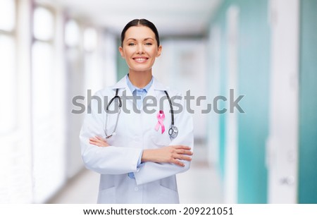 healthcare and medicine concept - smiling female doctor with stethoscope and pink cancer awareness ribbon over hospital background
