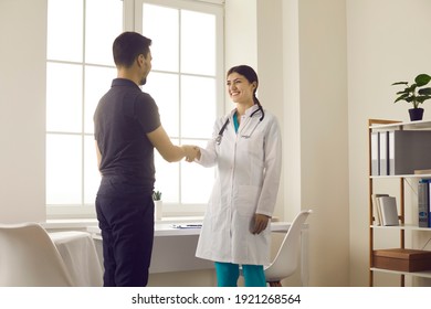 Healthcare And Medicine. Friendly Smiling Female Doctor Greets And Shakes Hands With Male Patient During Meeting In Medical Office. Concept Of Partnership, Trust And Medical Ethics.