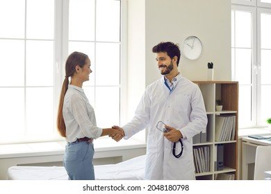 Healthcare And Medicine. Friendly Smiling Young Male Doctor Greets And Shakes Hand To Female Patient During Meeting In Medical Office. Concept Of Partnership, Trust And Medical Ethics.