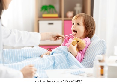 healthcare, medicine and people concept - doctor checking sick little girl's throat with tongue depressor in bed at home - Powered by Shutterstock