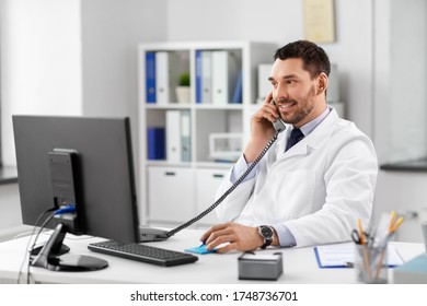 healthcare, medicine and people concept - smiling male doctor with clipboard calling on desk phone at hospital - Powered by Shutterstock