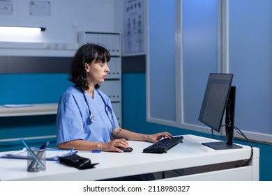 Healthcare Nurse Working With Monitor And Keyboard In Doctors Office. Medical Assistant Using Computer With Technology For Professional Support And Assistance, Working Late At Night.