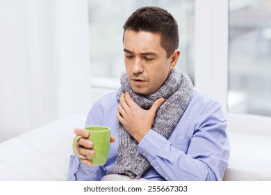 Healthcare, People And Medicine Concept - Ill Man With Flu Coughing And Drinking Hot Tea From Cup At Home