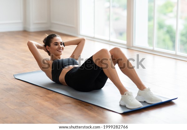 Healthcare,\
Physical Activity And Sports. Fit Young Lady Exercising At Fitness\
Club Studio Or Living Room Doing Sit-Ups Crunches Exercise Indoors\
Lying On Yoga Mat, Training Abdominal\
Muscles