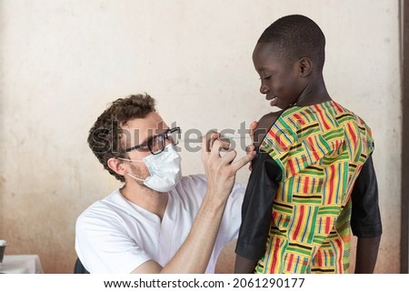 Healthcare profesional wearing a face mask carefully preparing antimalarial vaccination in a small black African schoolboy