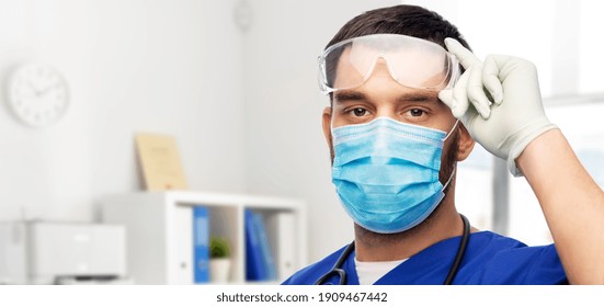 healthcare, profession and medicine concept - doctor or male nurse in blue uniform, face mask for protection from virus disease, goggles and gloves over medical office at hospital on background