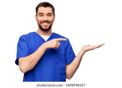 Healthcare, Profession And Medicine Concept - Happy Smiling Doctor Or Male Nurse In Blue Uniform Holding Something Imaginary On Empty Hand Over White Background