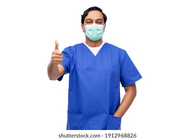 Healthcare, Profession And Medicine Concept - Indian Doctor Or Male Nurse In Blue Uniform And Face Protective Medical Mask For Protection From Virus Disease Showing Thumbs Up Over White Background