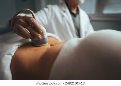 A healthcare professional conducts an ultrasound on a pregnant Caucasian woman, utilizing a transducer over her belly in a clinical setting. - Powered by Shutterstock