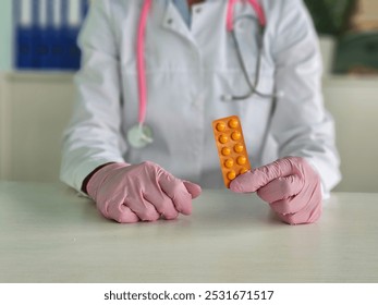 Healthcare professional in gloves holds orange medication pill blister pack in a medical office during daytime - Powered by Shutterstock