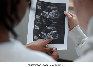 Healthcare professional holding and showing ultrasound images during prenatal checkup illustrating baby development and monitoring health progress without any medical apparatus in view - Powered by Shutterstock