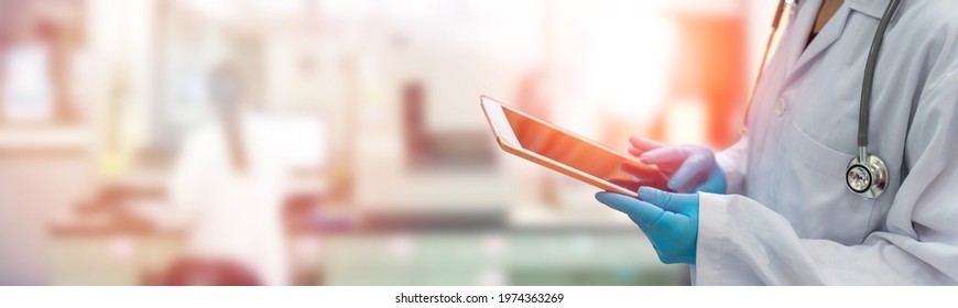 Healthcare professional medical doctor with stethoscope hand using tablet online with blur scientist working in hospital laboratory background. E-healthcare technology digital health care concept. - Shutterstock ID 1974363269