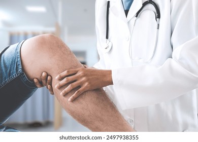 A healthcare professional in a white coat and a stethoscope is examining a patient's knee. The focus is on the hands of the doctor and the knee of the patient. - Powered by Shutterstock