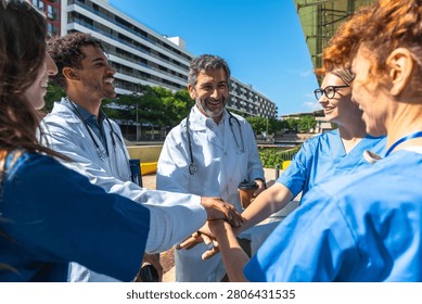 Healthcare professionals creating a stack of hands, symbolizing teamwork and synergy in the medical field, against an urban backdrop with a building under a clear sky