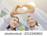 Healthcare professionals forming heart shape with hands. Blurred smiling faces of female pharmacists in white coats. Compassionate medical care concept in pharmacy setting. unity and teamwork.