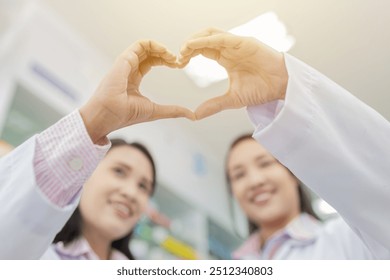 Healthcare professionals forming heart shape with hands. Blurred smiling faces of female pharmacists in white coats. Compassionate medical care concept in pharmacy setting. unity and teamwork. - Powered by Shutterstock