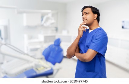 healthcare, stomatology and medicine concept - thinking indian doctor or male dentist in blue uniform over dental clinic office background