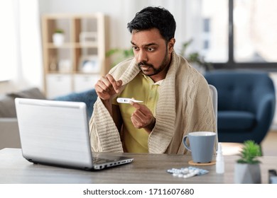 Healthcare, Technology And People Concept - Sick Indian Man In Blanket With Thermometer Having Video Call On Laptop Computer At Home